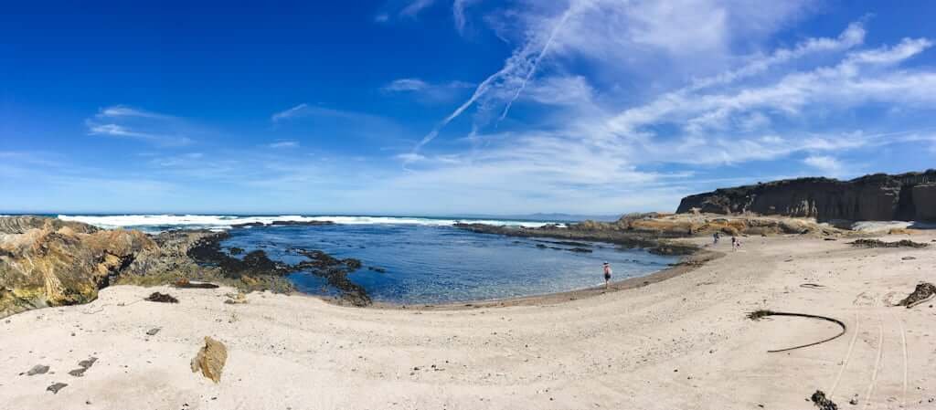 Montana de Oro beach with white sand and ocean cove with kid in foreground standing at water's edge