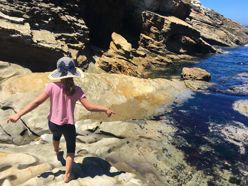 girl walking along smooth rocks in ocean inlet