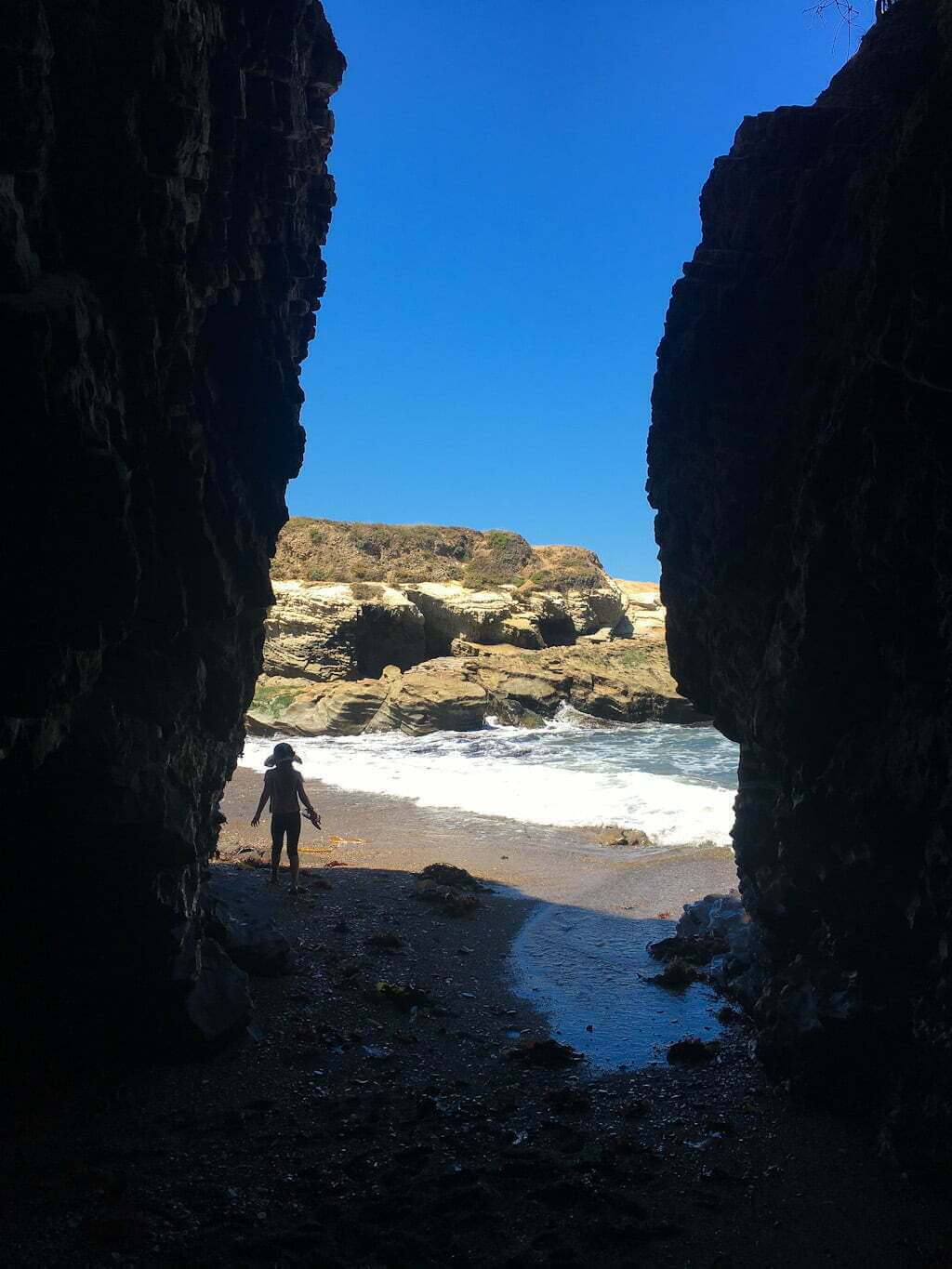 view out of sea cave towards beach with child's silhouette and rocks