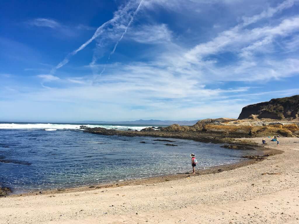 Montana de Oro beach with sand and sea cove with girl standing at water's edge