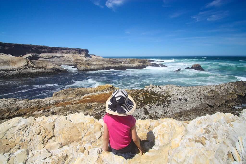 girl in sunhat sitting and viewing the ocean from rocks