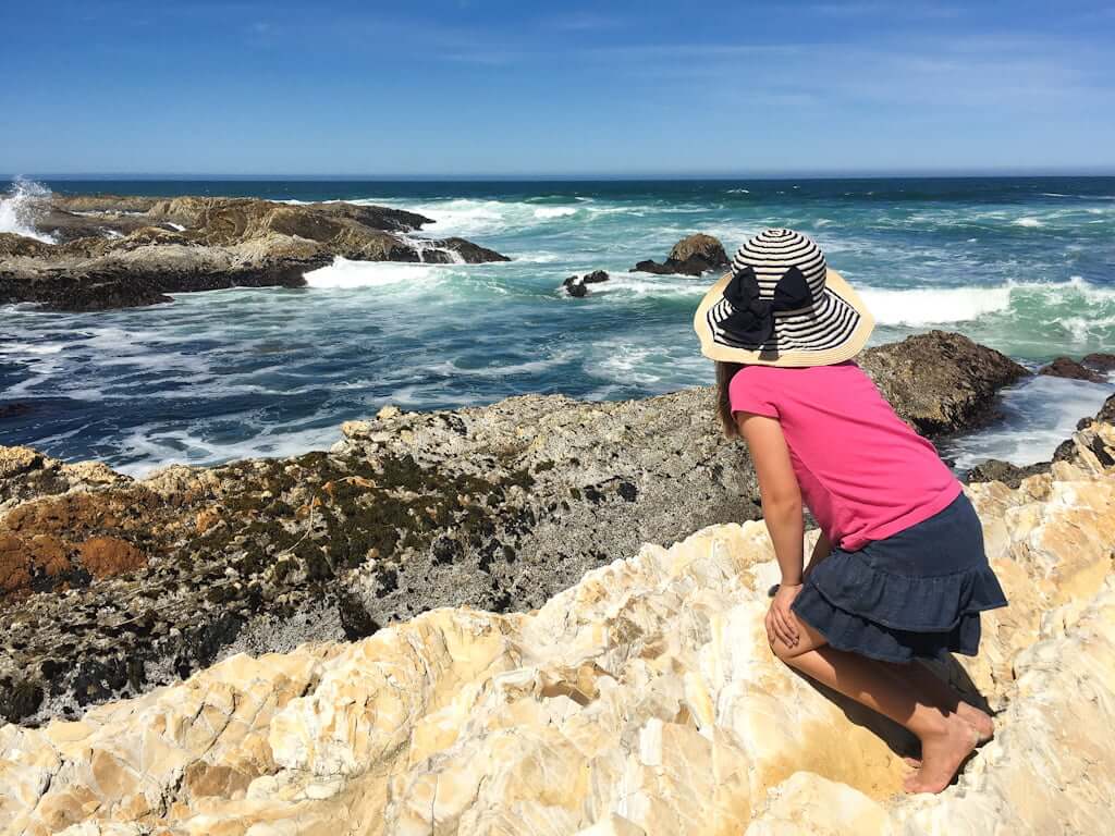 girl in sunhat looking out over the ocean from rocks