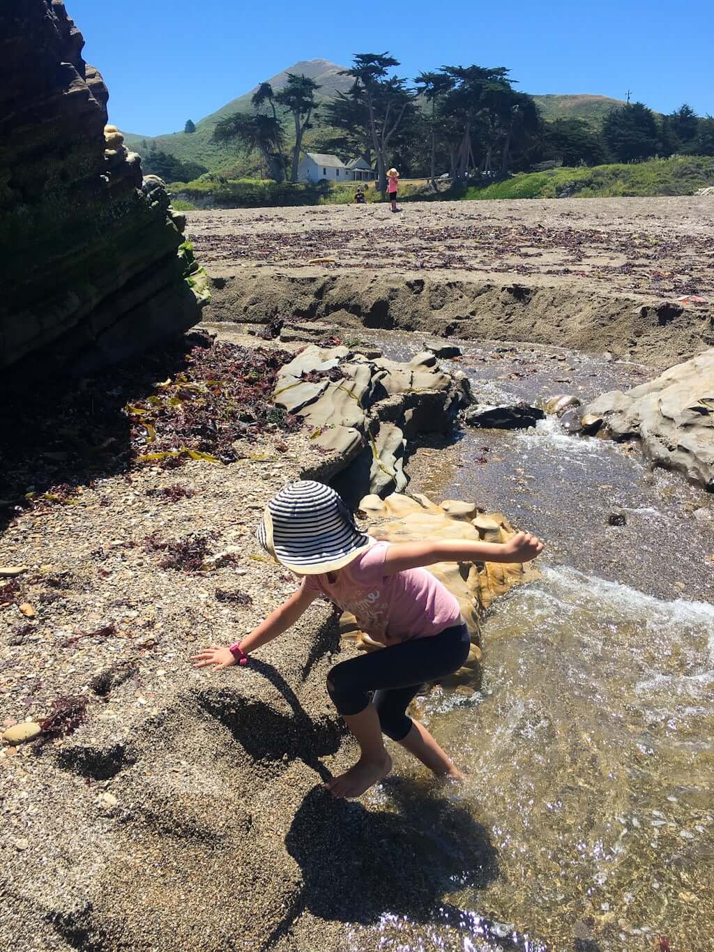 child playing in small river on rocky beach