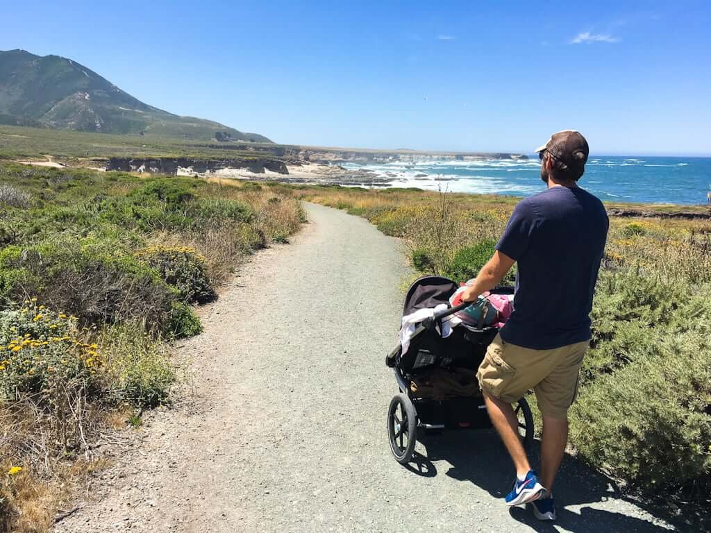 man pushing stroller down Bluff Trail in Montana de Oro with mountains in distance