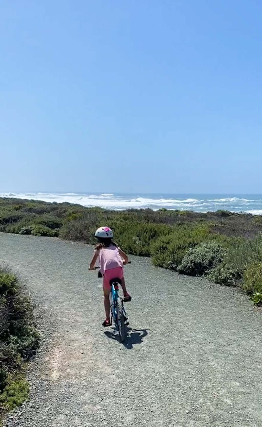 young girl biking along Montana de Oro trail with views of Pacific Ocean in distance