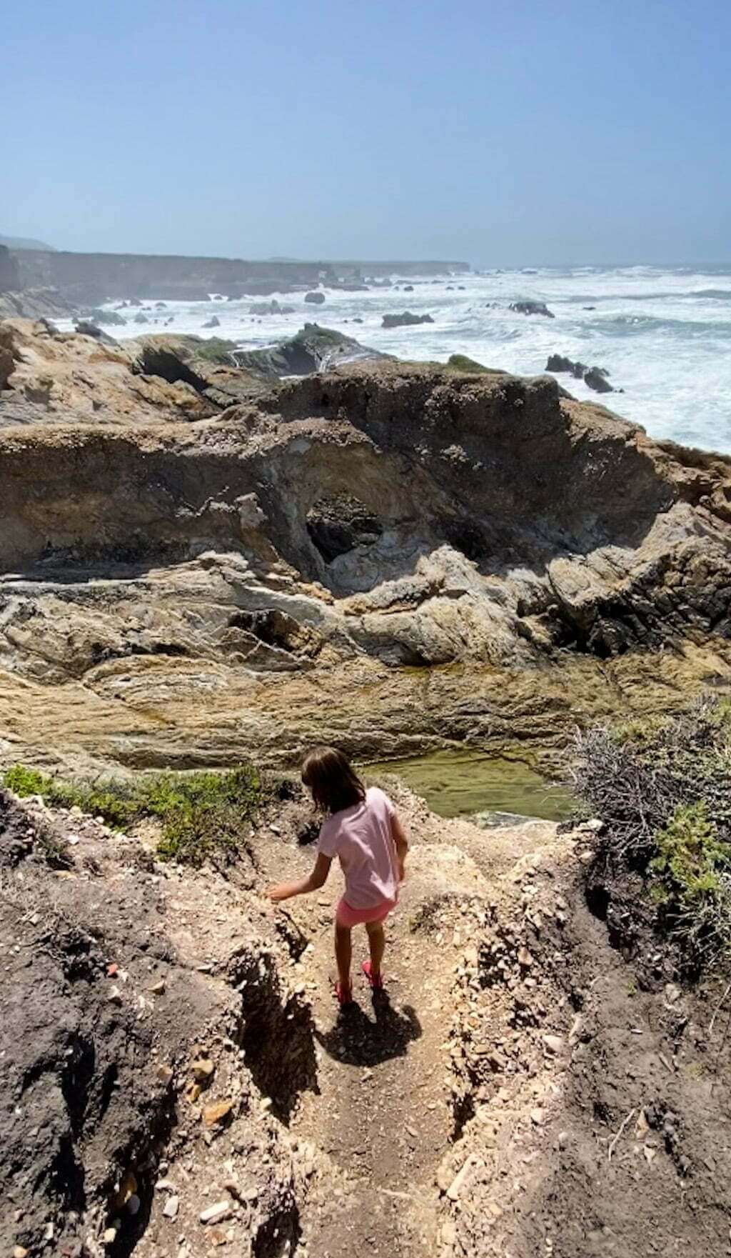 girl climbing down rocks next to ocean towards an arch in Montaña de Oro