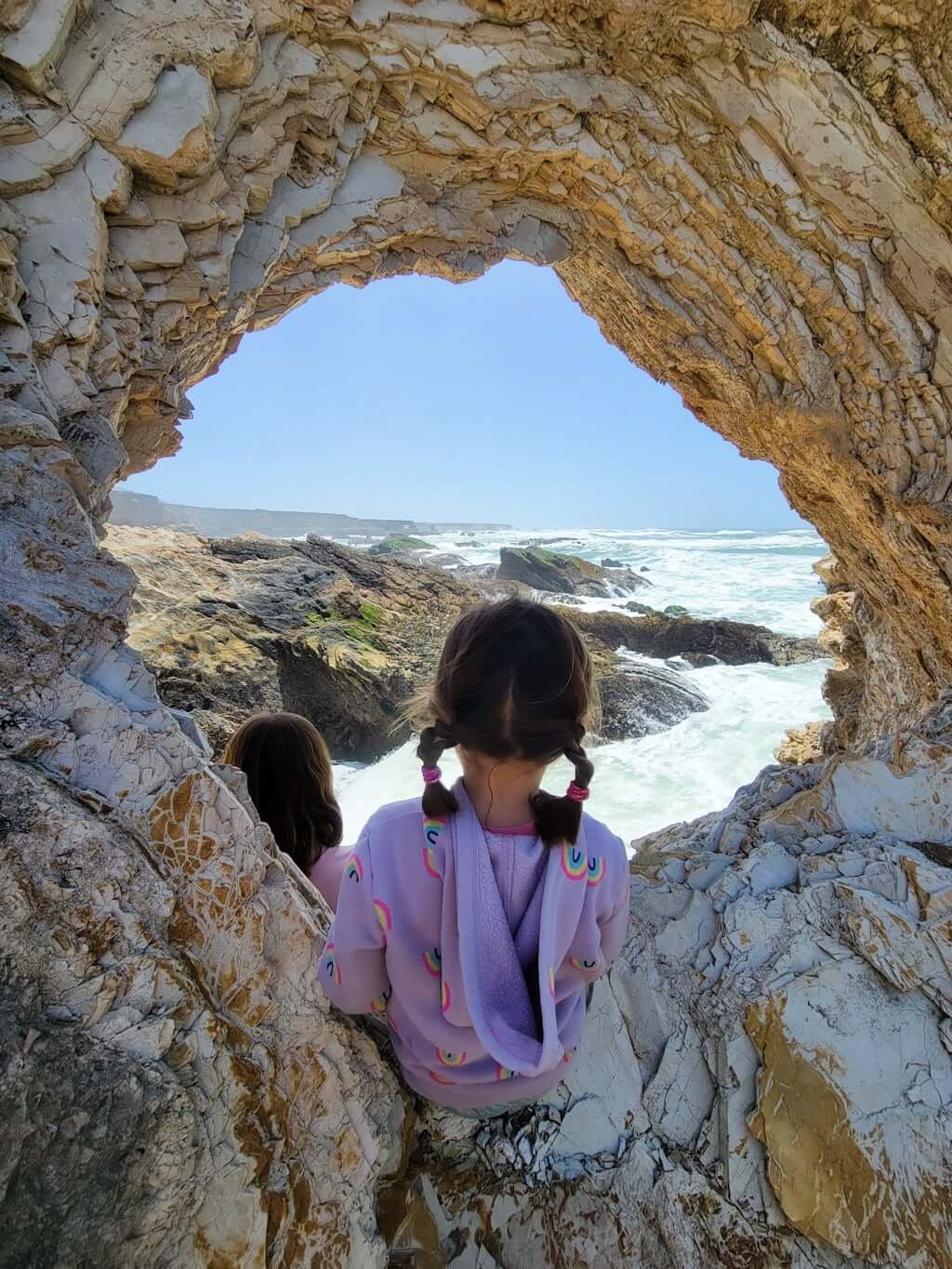 kids looking through arch in Montaña de Oro towards a view of coastline with ocean crashing into rocks for a distance