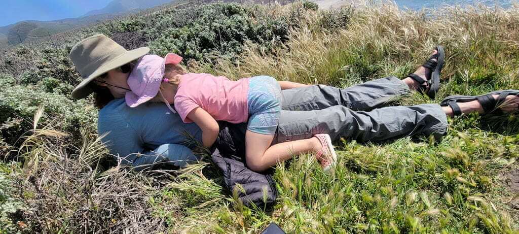 daughter cuddling mother in grass on clifftop