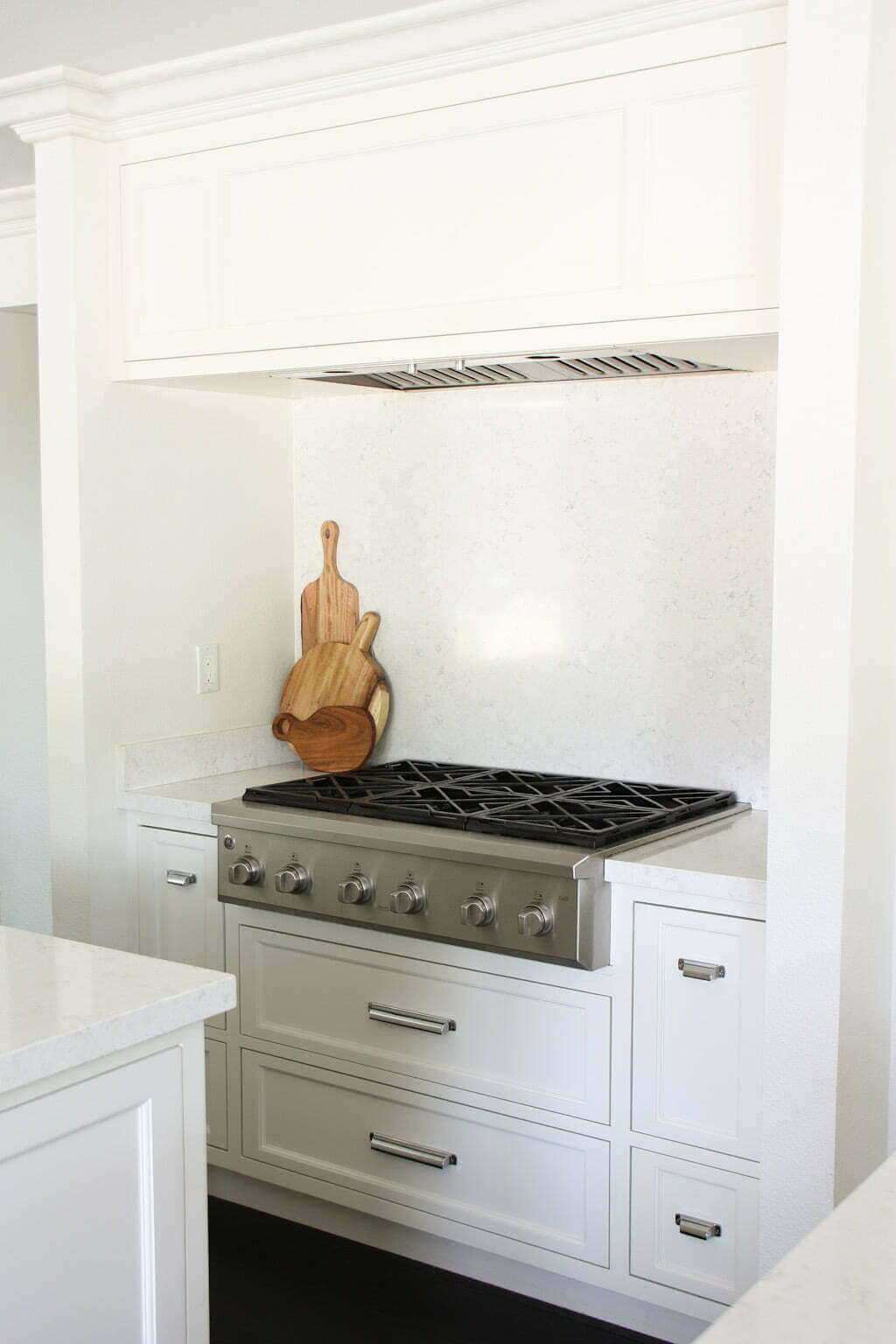 white kitchen stove area with drawers below, quartz backsplash solid, hood and white wood hood above, and gas stove