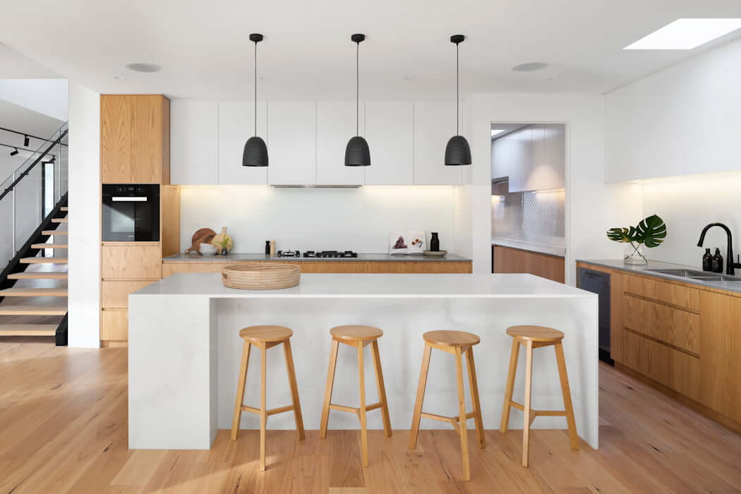 white simple kitchen with wood floors, island with wood barstools, black pendant lights from ceiling