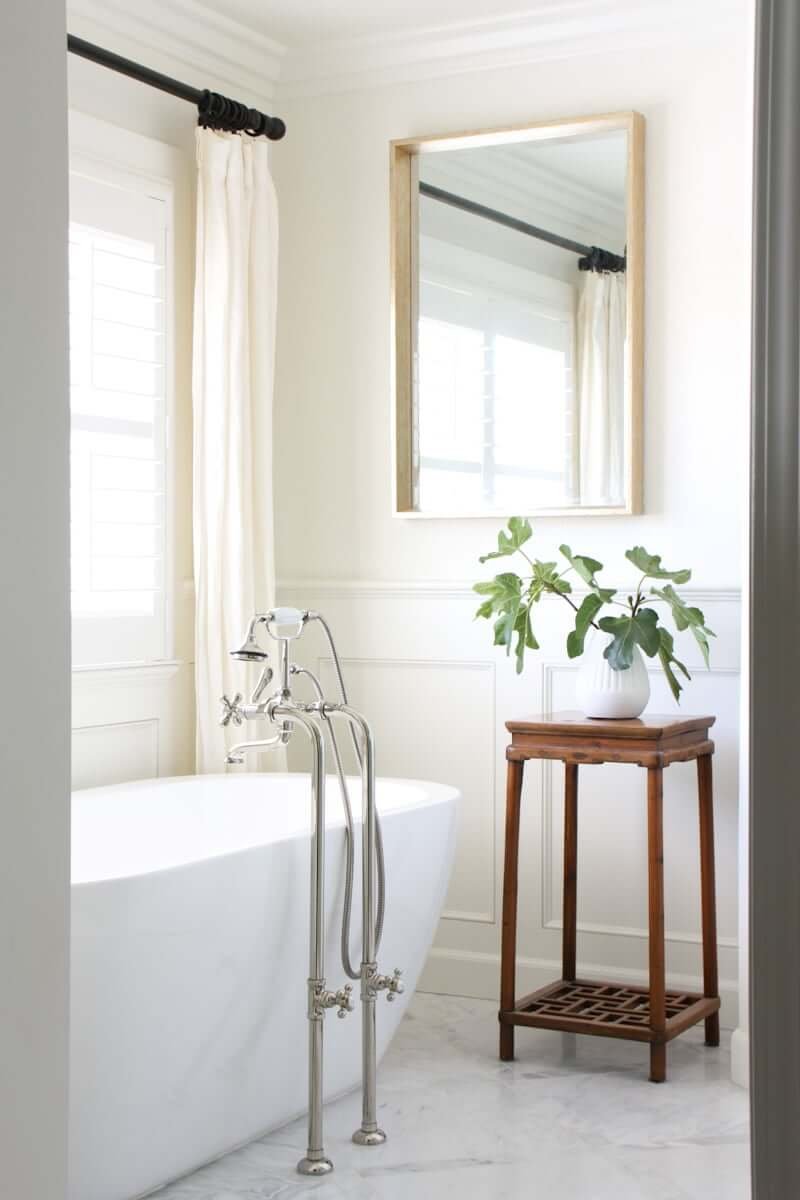 white marble bathroom with white tub and plant on plant stand