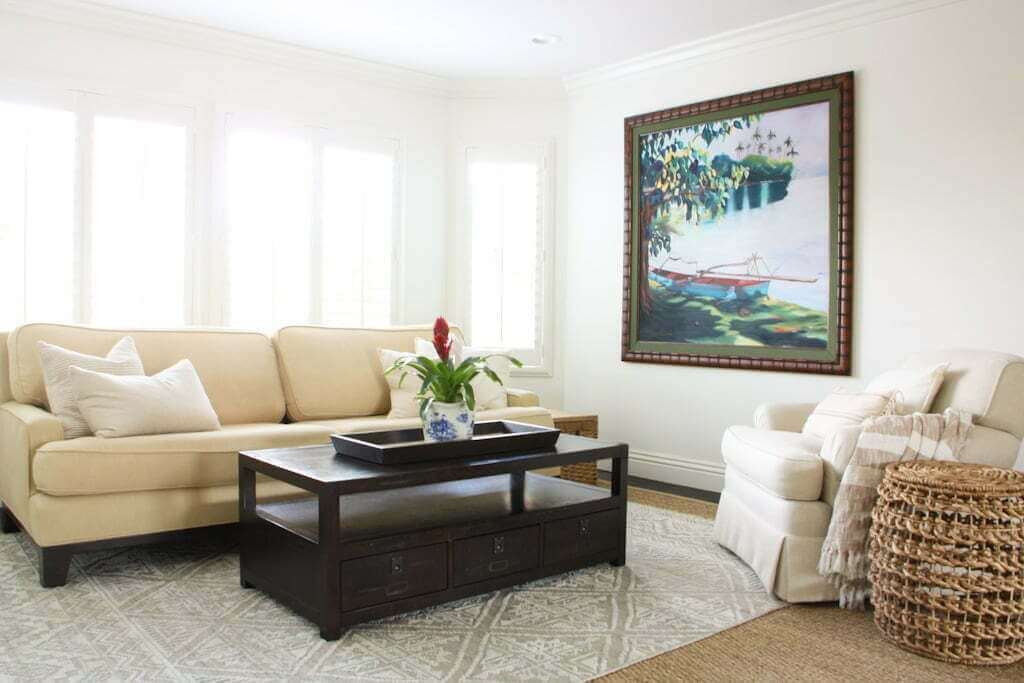 living room with tropical artwork, plants, and neutral seating and rugs with bay window