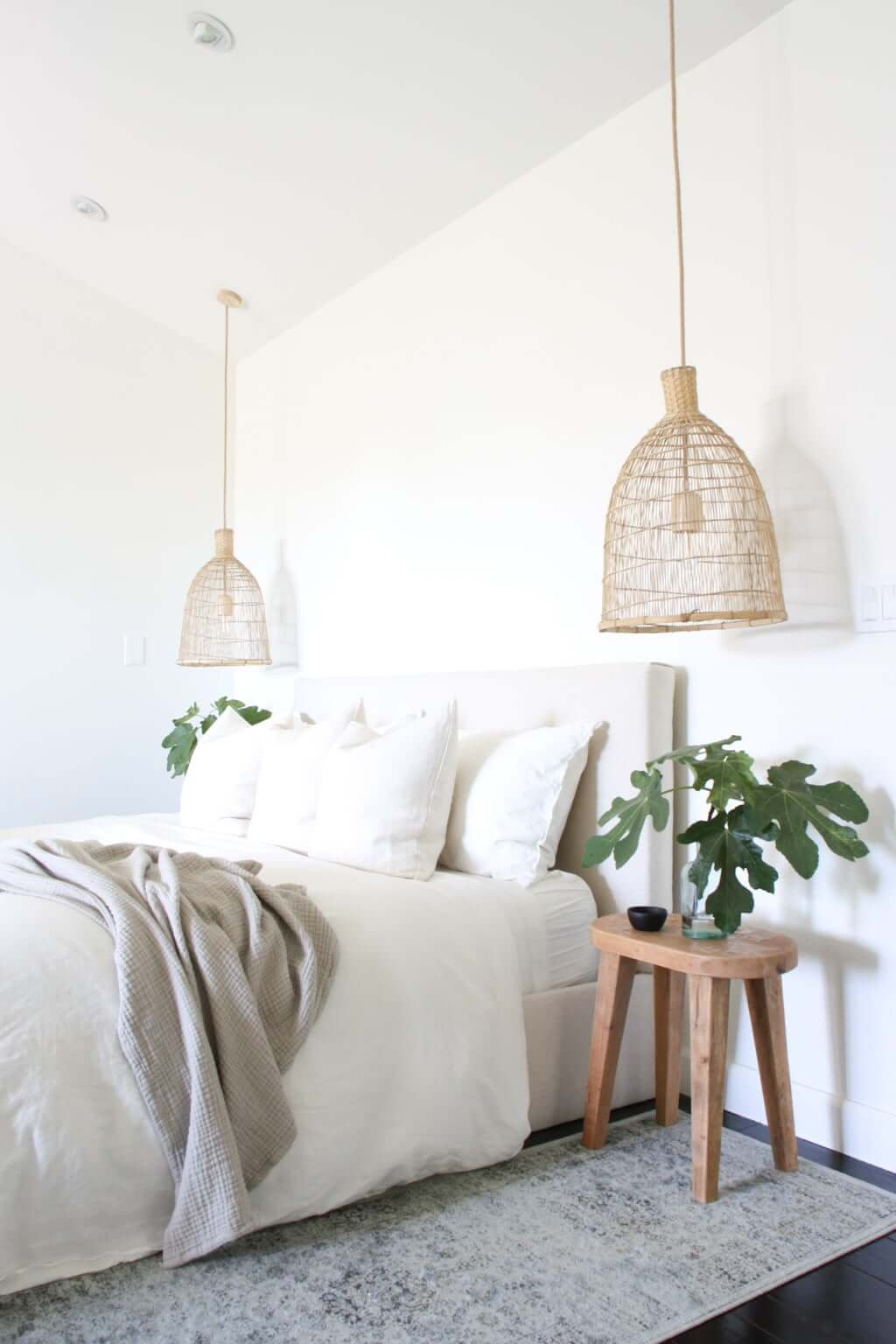 linen bed with wood side tables, plants, rugs, dark wood floors, and woven pendant lights bedside