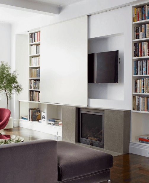 living room with tv hidden behind sliding panel above fireplace, and bookshelves on either side