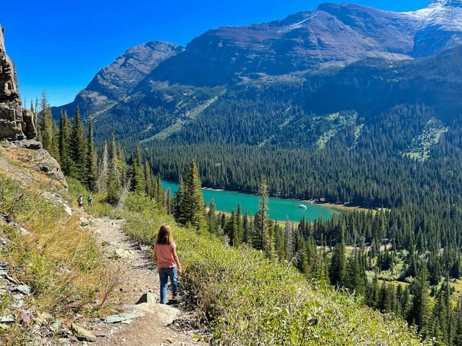 girl hiking in Glacier National Park with lake and mountains around