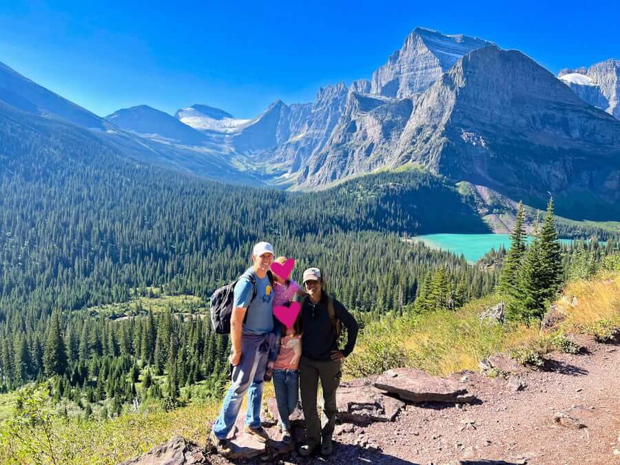 family on hike in Glacier National Park with kids with mountains and lake and trees in background