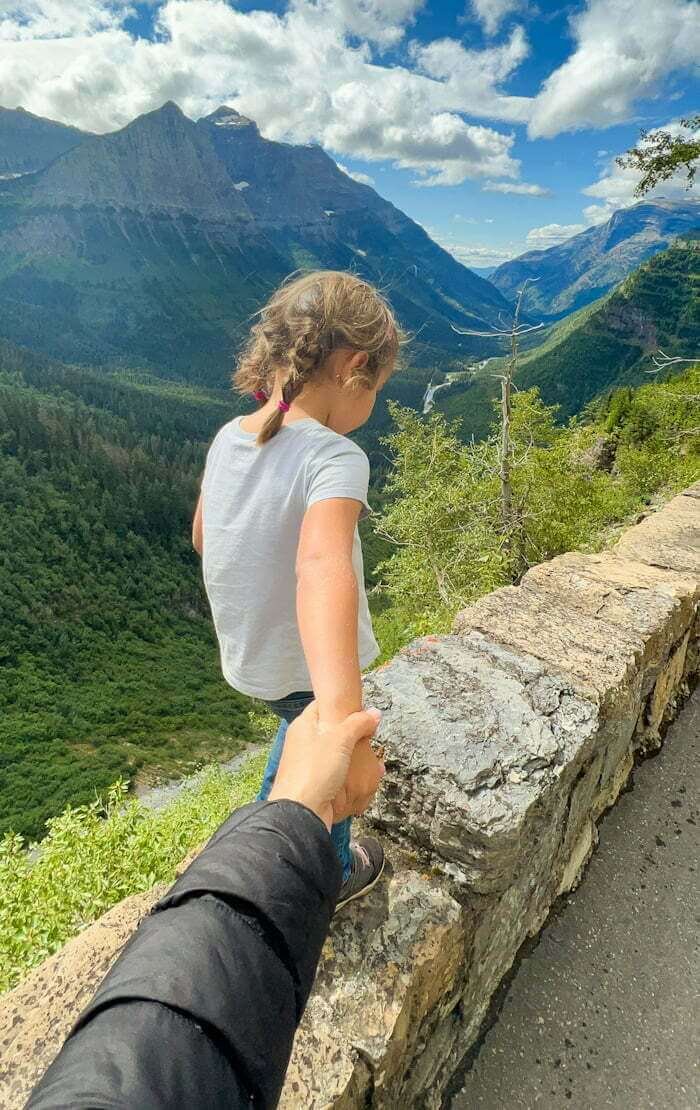 mother's hand holding child's hand while walking along wall along the Going-to-the-Sun Road viewpoint