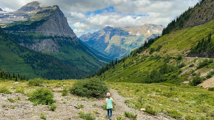 girl hiking along trail in Glacier National Park with Going-to-the-Sun Road in distance