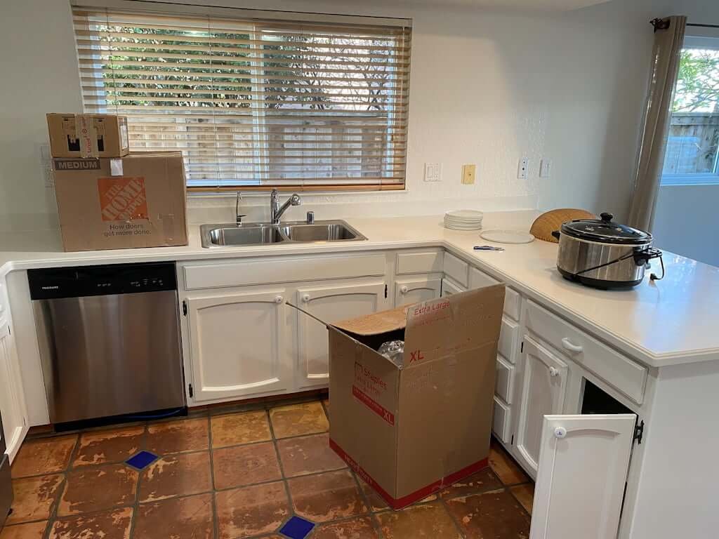 small white kitchen with tile floors and moving boxes