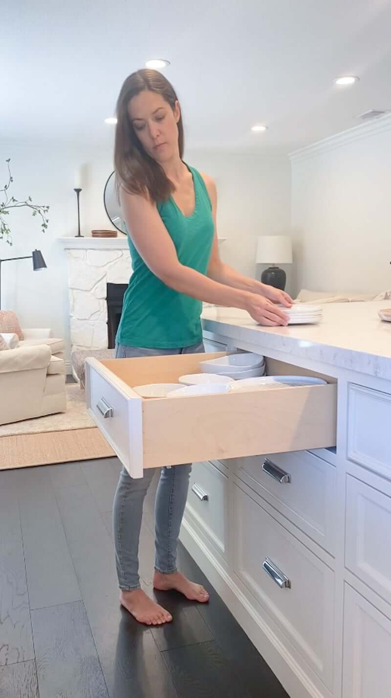 woman in kitchen, storing plates in a drawer