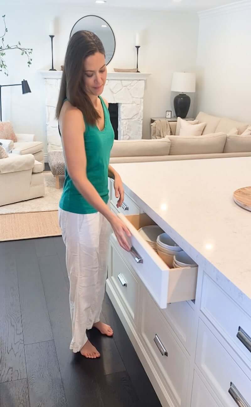 women in kitchen opening a drawer full of plates stored inside
