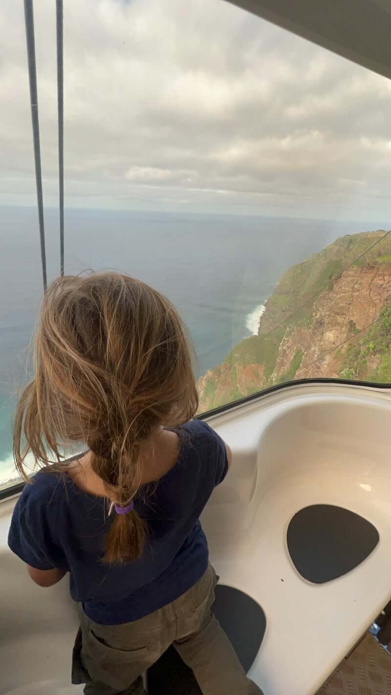 girl looking out window of cable car going down cliff overlooking the ocean