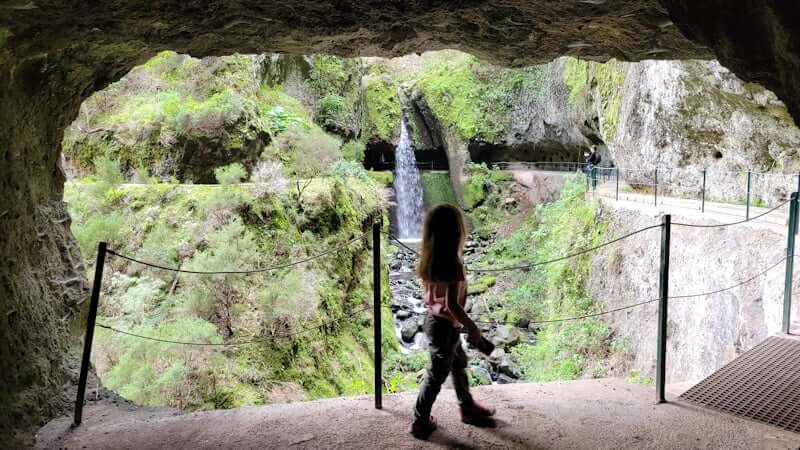 girl walking in levada tunnel looking towards a waterfall