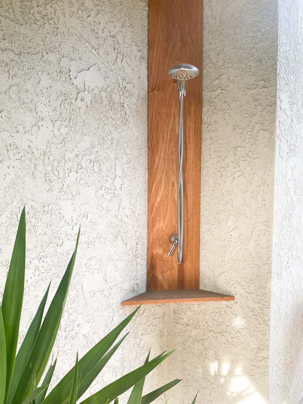 Simple outdoor shower cost with wood and chrome shower head and plants for privacy 