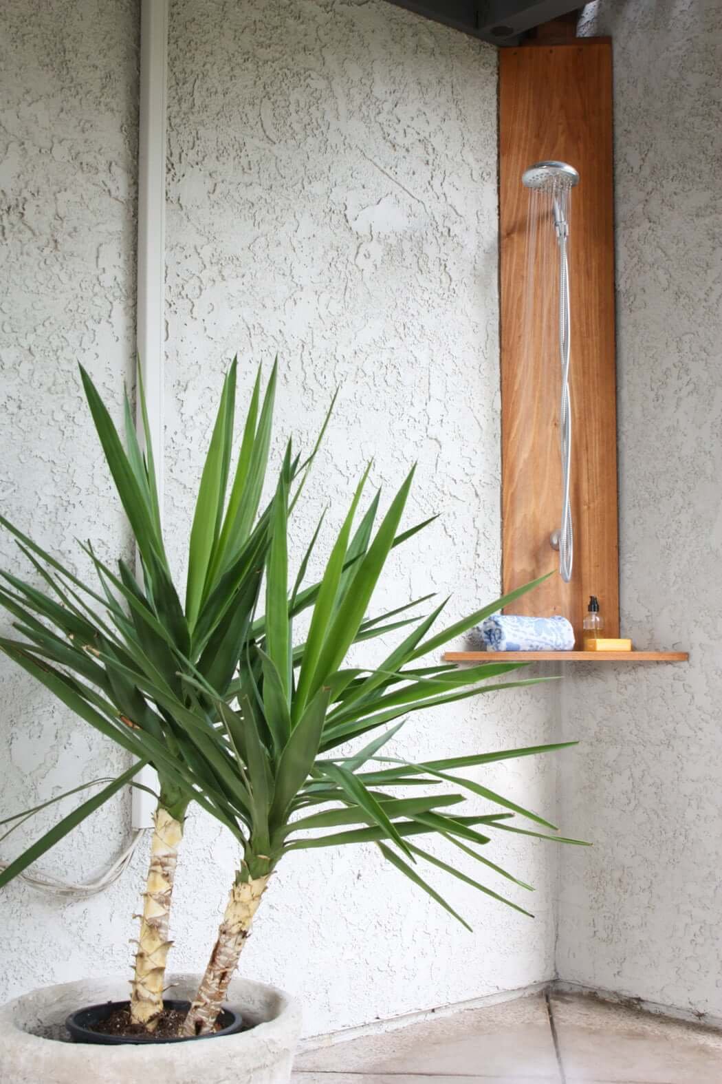 Outdoor shower made of wood and chrome shower head, with shelf below with towel, shampoo and soap