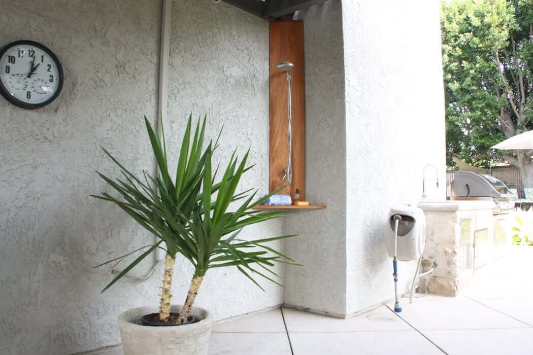 backyard with DIY outdoor shower in corner and outdoor kitchen and patio in background