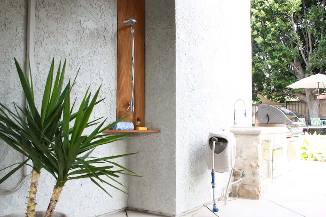 DIY outdoor shower in backyard corner with plumbing and hose and plants 