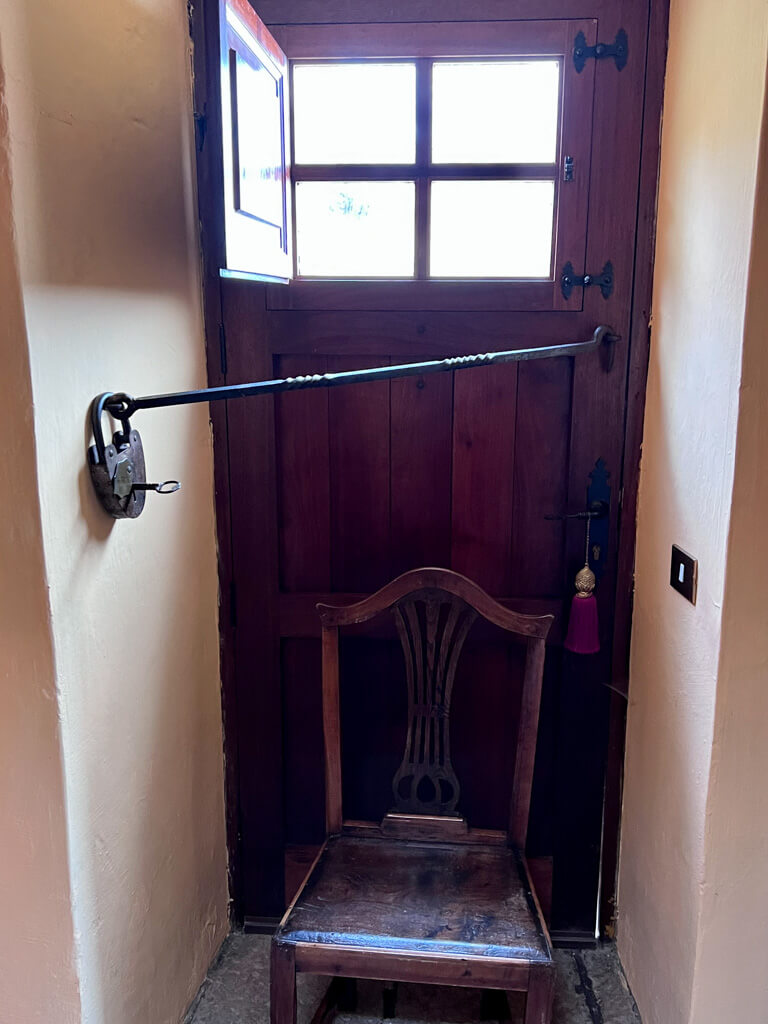 Door with large iron bar slanting across to large lock and chair in front of the door. 