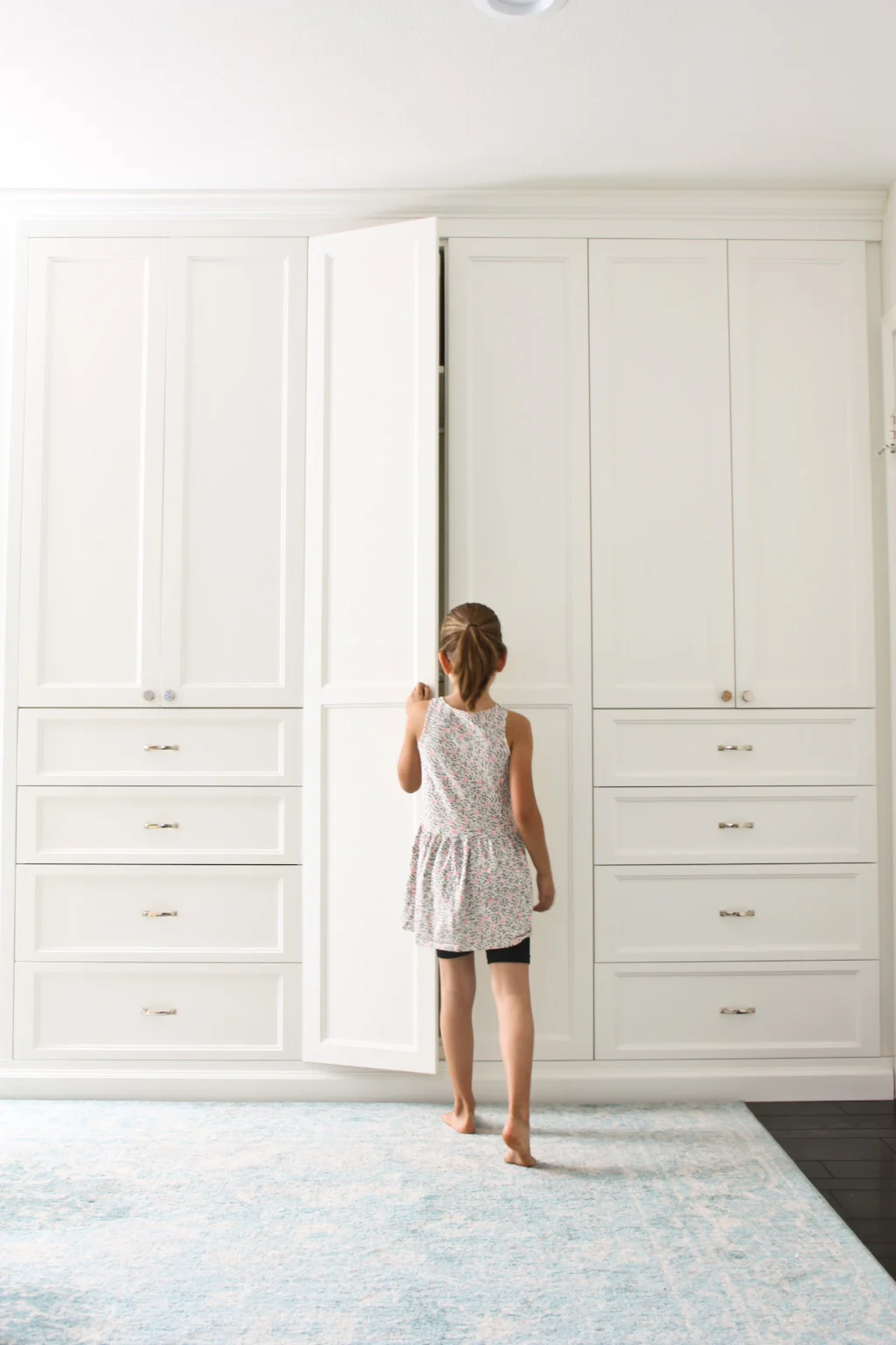Guest bedroom closet ideas. White closet built-ins with drawers. Rug on the ground in front of the built in closet.