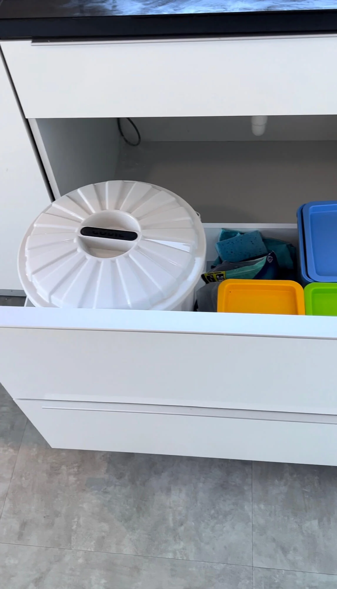 Under sink storage idea with a pull out drawer that holds a trashcan and cleaning supplies 