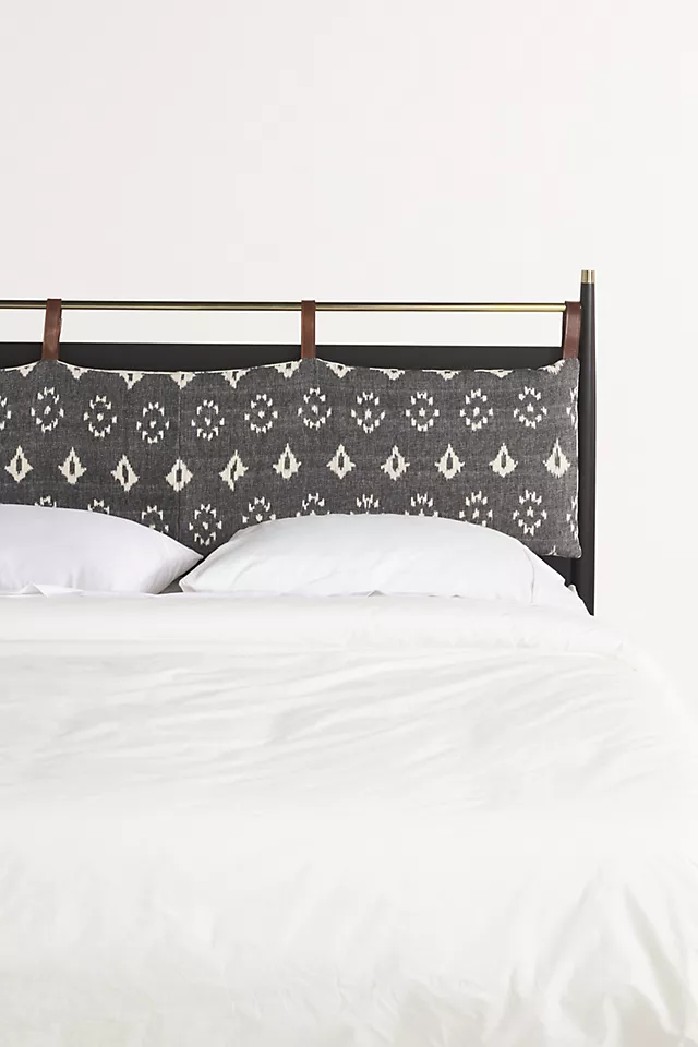 Black wooden bed headboard with a beautiful patterned headboard cushion attached to it and white bedding on the bed.