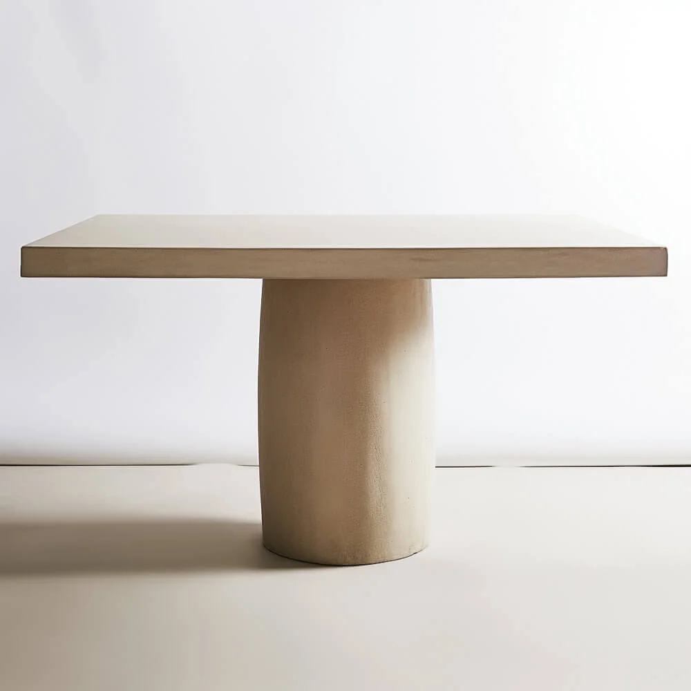 A rectangular plaster dining table with a singular, round base. 