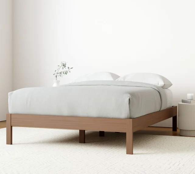 Minimalist wooden bed frame design in a room with white walls and a white rug below the bed.