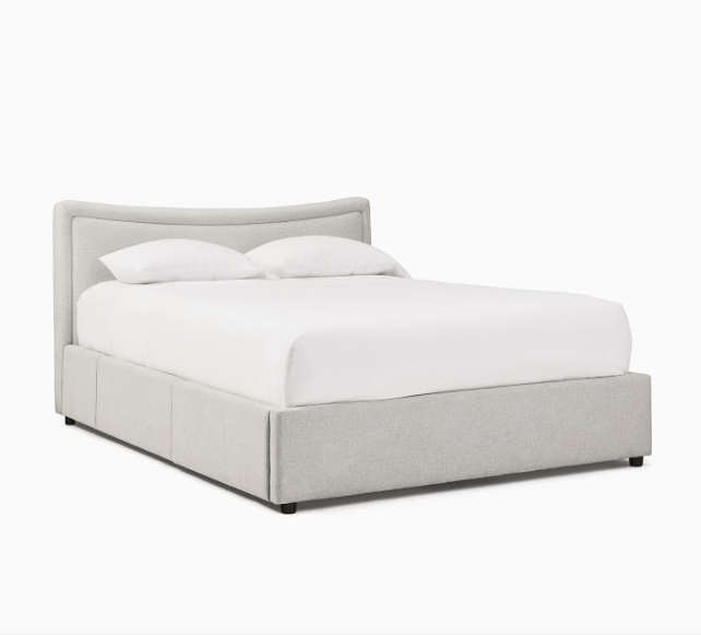 A curved upholstered bed frame with storage and white bedding.