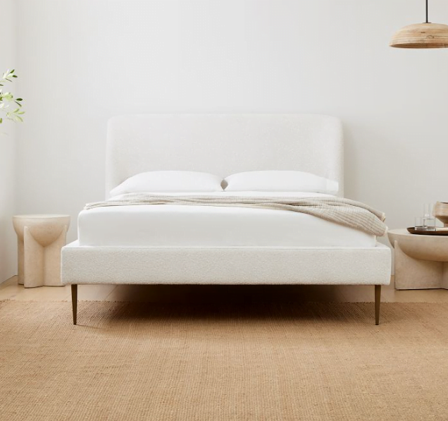 A white upholstered bed frame design with wooden legs and a jute rug below the bed. 