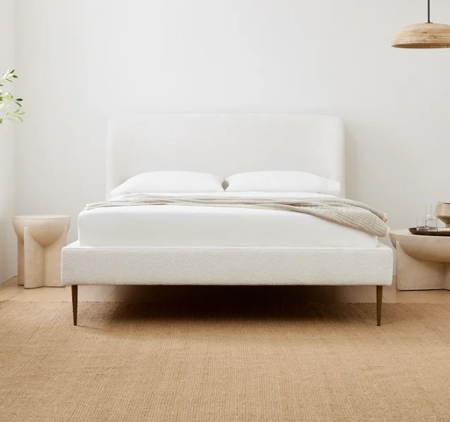 A white upholstered bed frame design with wooden legs and a jute rug below the bed.