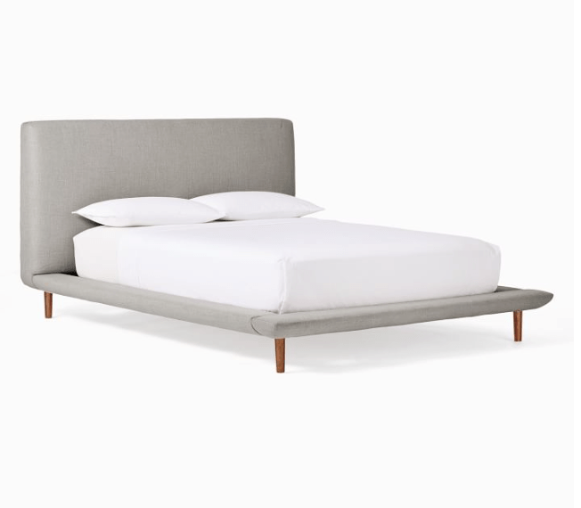Upholstered platform bed frame design with wooden legs and white bedding.