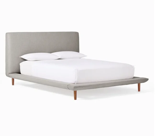 Upholstered platform bed frame design with wooden legs and white bedding.