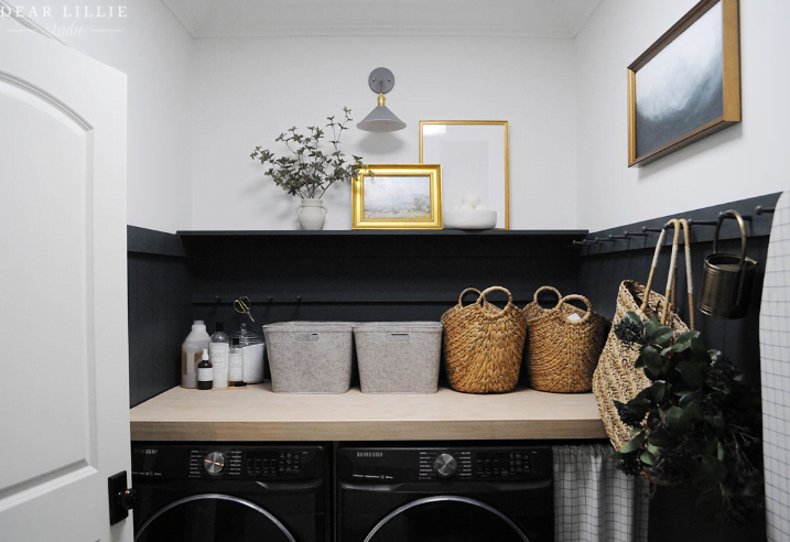 Small laundry room decor ideas with hooks as laundry room wall decor. Artwork hangs above the hooks and baskets sit on top of the washer and d ryer. 