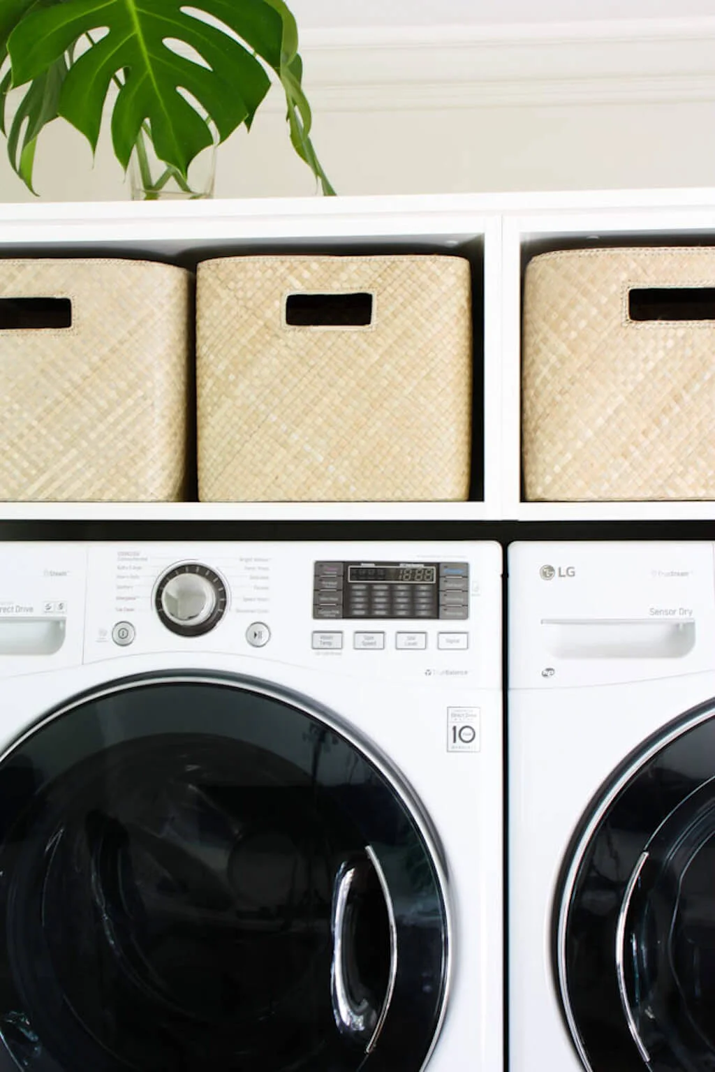 Small laundry room decor ideas of a built in shelving unit that hold washer and dryer. Wicker baskets sit on the top shelf.