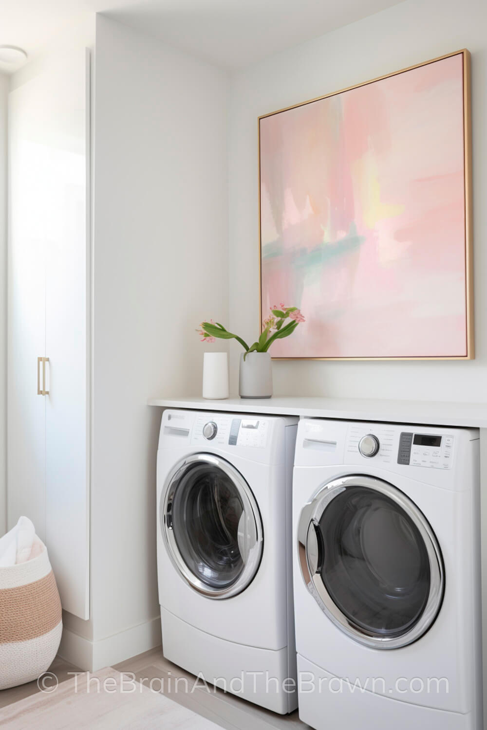 A large piece of laundry room wall decor hangs above a washer and dryer. A plant sits on the washer and dryer. Modern laundry room decor ideas