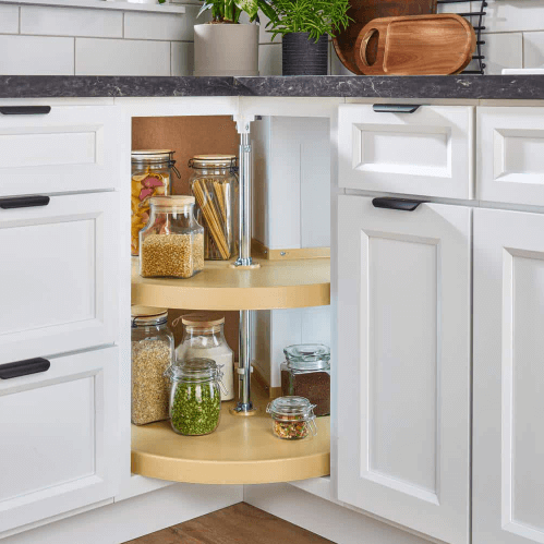 A lazy susan in a corner cabinet of a kitchen with white kitchen cabinets and black countertops.