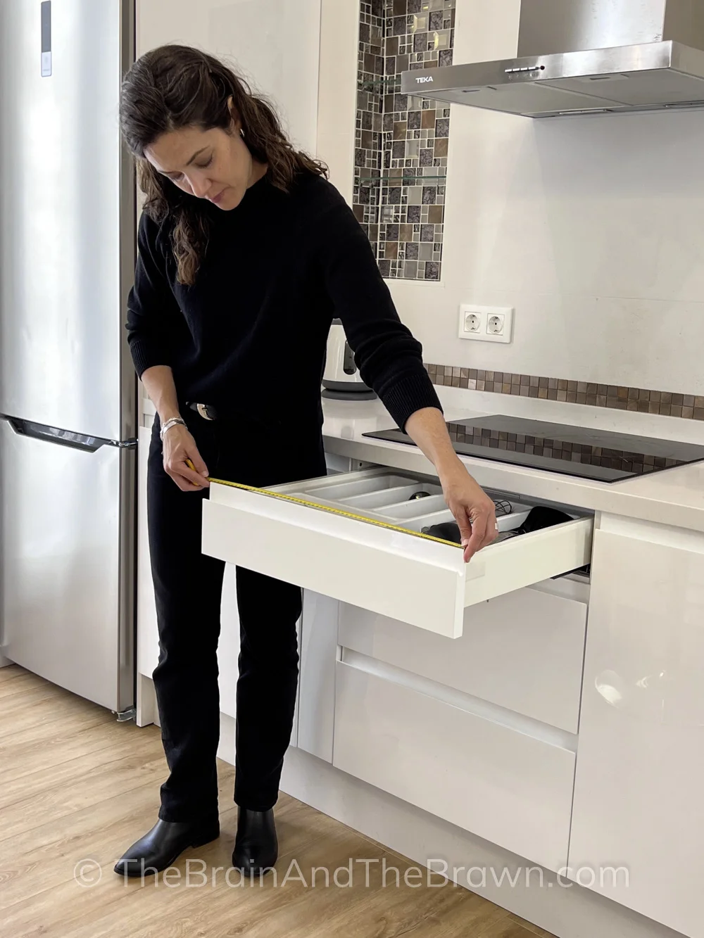 A woman stands in a kitchen measuring a drawer