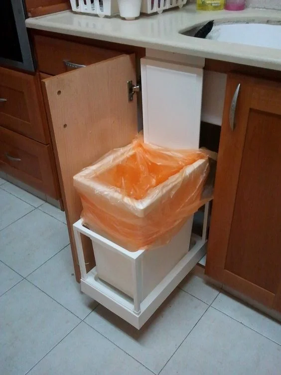 A pull-out trash bin behind a kitchen cabinet door.