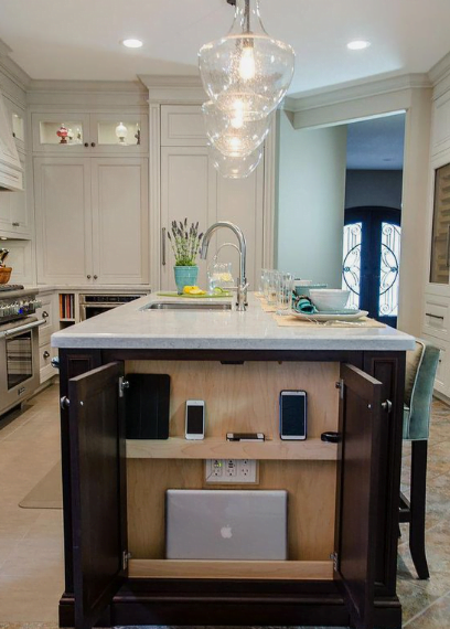 An open narrow cabinet at the end of a kitchen island with storage for storing and charging electronic devices