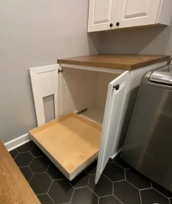 A pull out kitchen shelf inside a white cabinet. Black hexagon tile on the floor. 